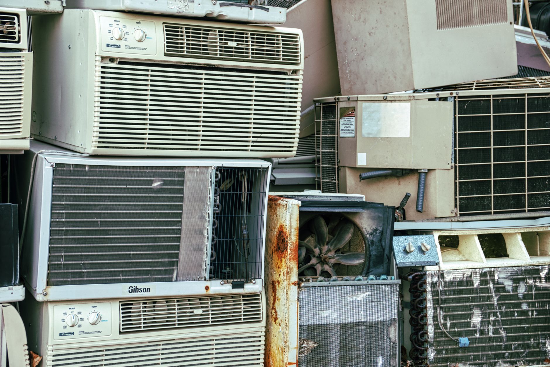 A collection of broken and rusted air conditioners piled in an outdoor junkyard, similar to what happens to old appliances in Port St Lucie without proper pickup.