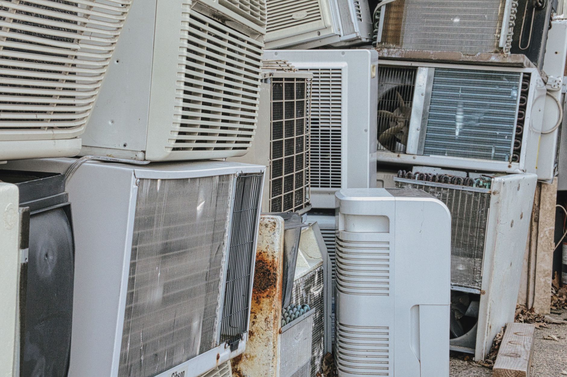 A collection of various old and broken air conditioning units piled outdoors, an example of the appliance types picked up in Port St Lucie.